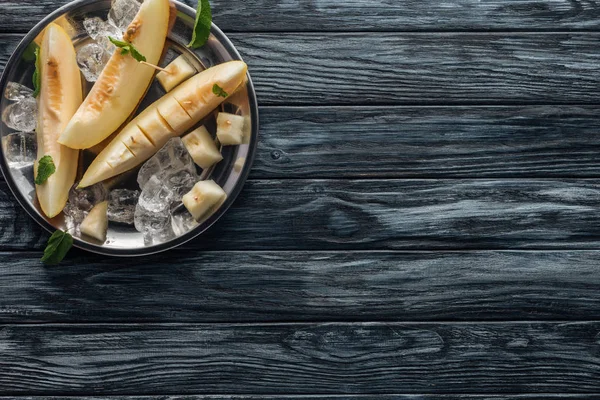 Vista dall'alto del melone fresco affettato dolce con cubetti di ghiaccio e menta sulla superficie di legno — Foto stock