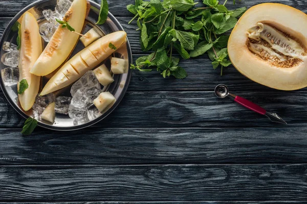 Vista dall'alto di melone dolce maturo con cubetti di ghiaccio e menta sulla superficie di legno — Foto stock