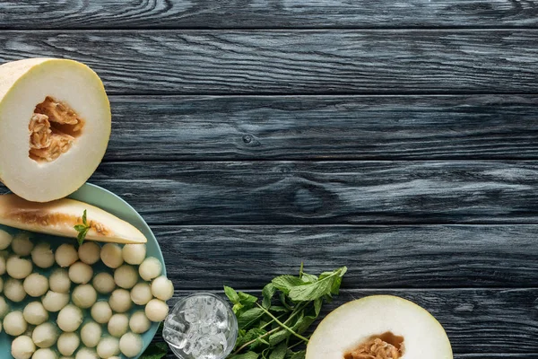 Vue de dessus de délicieux melon sucré mûr, glaçons, menthe et boules de melon sur la surface en bois — Photo de stock