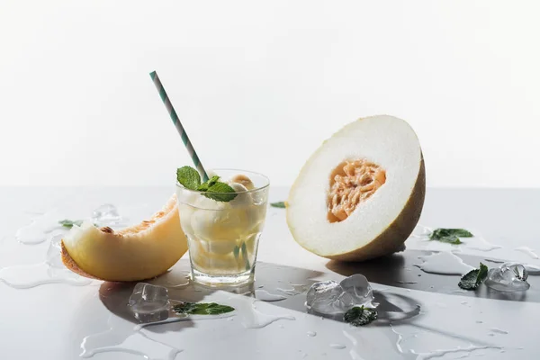 Bebida de verano con menta y melón en vidrio, cubitos de hielo derretido y melón maduro dulce sobre blanco - foto de stock