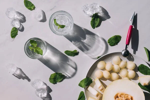Boules de melon sucrées, moitié melon mûr et boisson rafraîchissante à la menthe et pailles à boire dans des verres sur blanc — Photo de stock