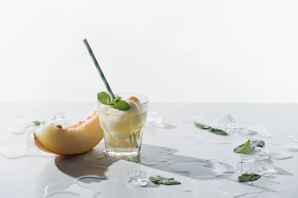 Vista de cerca de la bebida de verano con melón y menta en vidrio y rebanada de melón dulce con cubitos de hielo en blanco - foto de stock