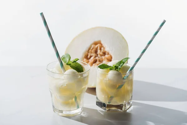 Vista close-up de bebida de verão com melão e hortelã em óculos e metade de melão maduro em branco — Fotografia de Stock