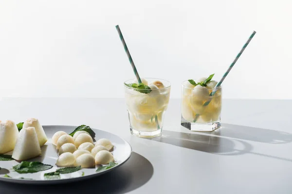 Süße Melonenbällchen und erfrischendes Getränk mit Melone und Minze in Gläsern auf weiß — Stockfoto