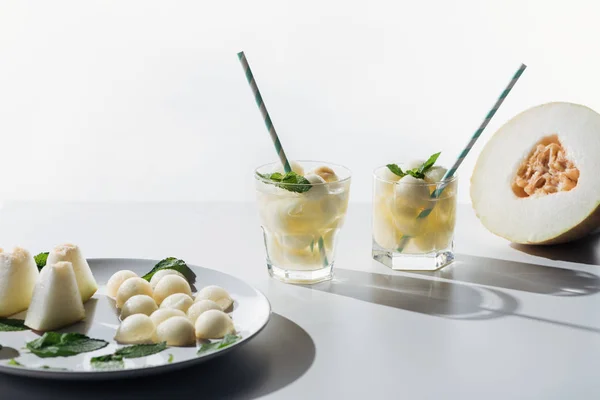 Vue rapprochée des boules de melon sucrées et des boissons rafraîchissantes au melon et à la menthe dans des verres sur blanc — Photo de stock