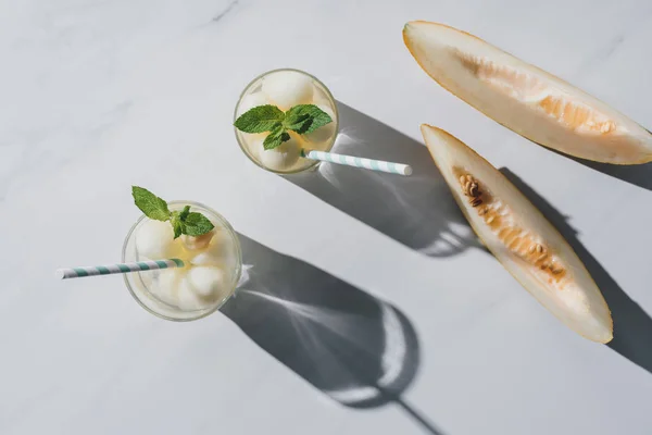 Vue de dessus de boisson rafraîchissante avec melon et menthe dans des verres et des tranches de melon mûr sur blanc — Photo de stock