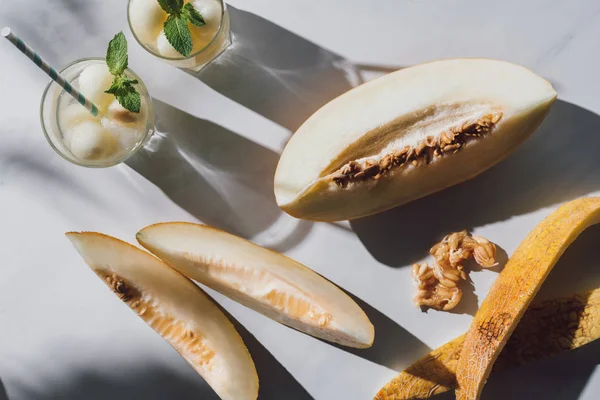 Vue de dessus de melon mûr délicieux, verres avec boisson rafraîchissante et graines sur blanc — Photo de stock