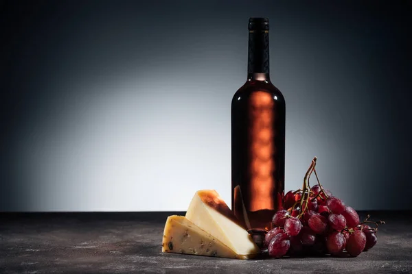 Bottle of red wine, different types of cheeses and grapes on wooden table — Stock Photo