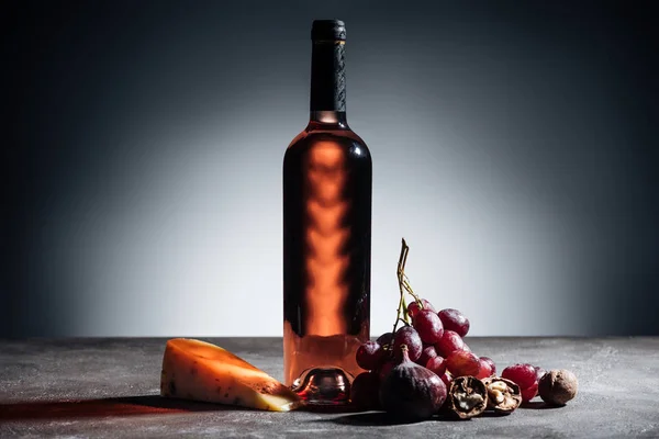 Bottiglia di vino rosso, pezzo di formaggio e uva su grigio — Foto stock