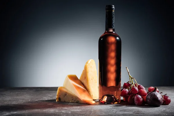 Flasche Rotwein, verschiedene köstliche Käsesorten und Trauben auf grauem Grund — Stockfoto