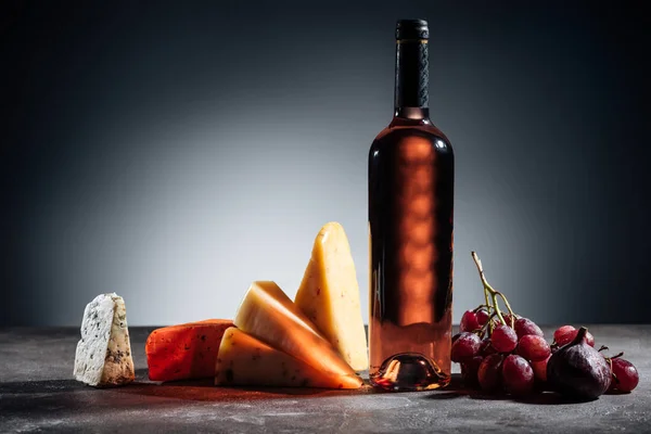 Botella de vino tinto, diferentes tipos de quesos y uvas sobre gris - foto de stock