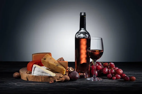 Bottle of red wine, wineglass and different types of cheeses on grey — Stock Photo