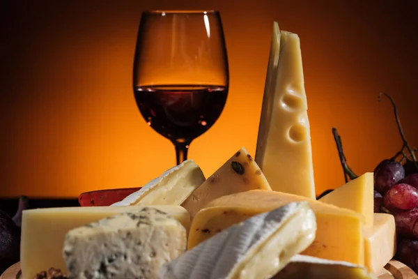 Different types of appetizing cheeses and glass of wine on orange — Stock Photo