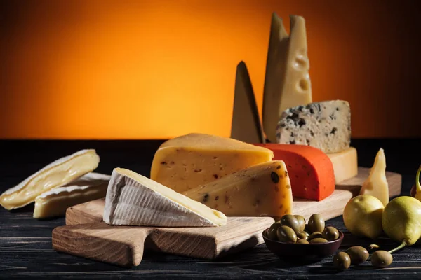 Different types of appetizing cheeses on cutting board on orange — Stock Photo