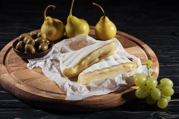 Delicioso queijo brie, uvas, peras e azeitonas na tábua de corte — Fotografia de Stock