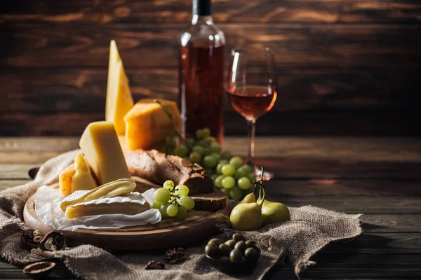 Different types of cheeses, grapes and pears on rustic tablecloth — Stock Photo