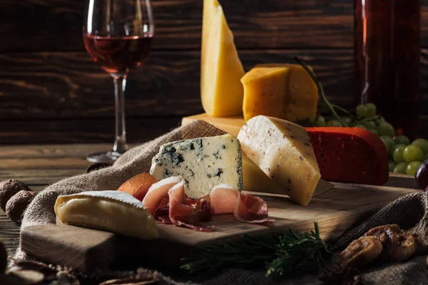 Different types of cheeses and prosciutto on wooden board — Stock Photo