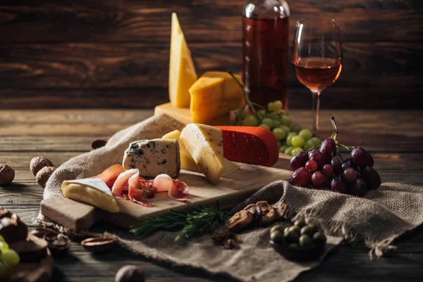 Différents types de fromages, prosciutto et raisins sur nappe rustique — Photo de stock
