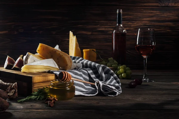 Different types of cheeses, honey with stick and wine on table — Stock Photo