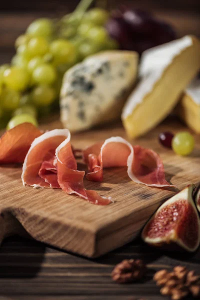 Prosciutto sobre tábua de corte com queijos sobre fundo — Fotografia de Stock