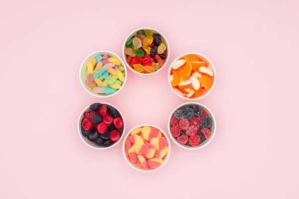 Vista superior de vasos de papel con deliciosos caramelos de gelatina en círculo aislado en rosa - foto de stock
