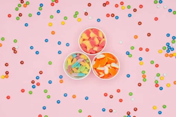 Top view of paper cups with jelly candies and scattered dragee isolated on pink — Stock Photo