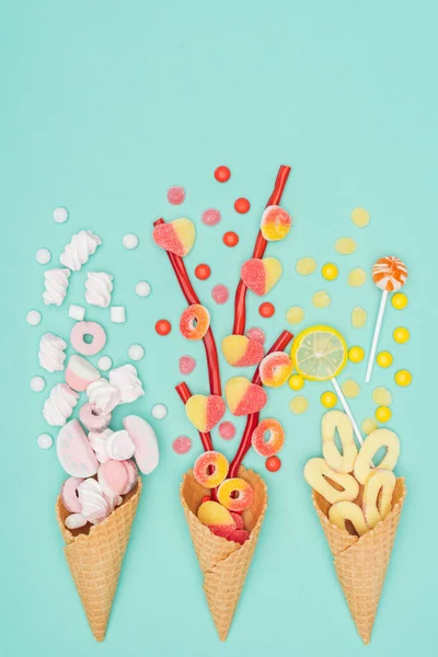 Vue de dessus des bonbons à la gelée, guimauves, sucettes et cônes de gaufres isolés sur turquoise — Photo de stock