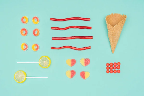 Flat lay of jelly candies, dragee, lollipops and waffle cone isolated on turquoise — Stock Photo