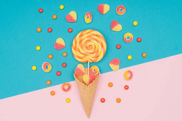 Vista dall'alto di caramelle alla gelatina, lecca-lecca e cono di cialda su superficie blu e rosa — Foto stock