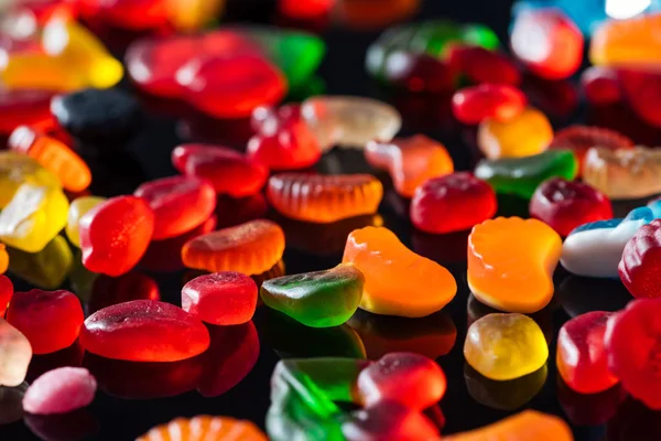 Doces de geleia brilhantes saborosos na superfície preta — Fotografia de Stock