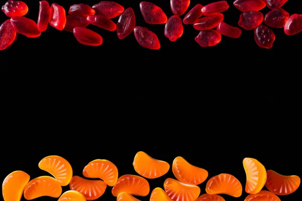 Vue de dessus des bonbons en gelée en forme de lèvres et de morceaux de mandarine isolés sur noir — Photo de stock