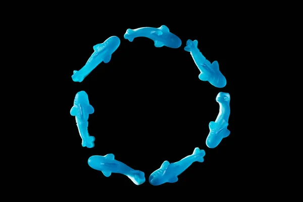 Top view of circle of blue jelly candies in shape of dolphins isolated on black — Stock Photo