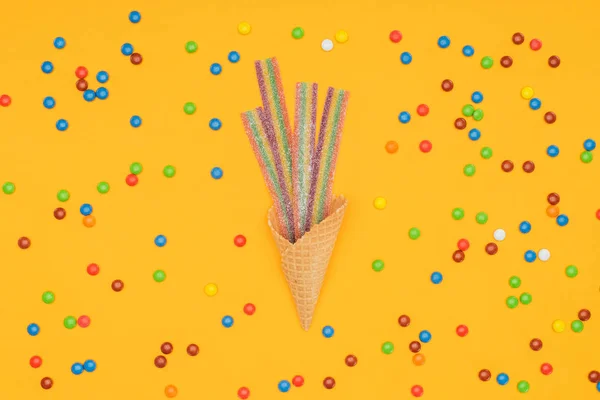 Vista superior de caramelos planos de gelatina en cono de gofre y dragee disperso aislado en naranja - foto de stock