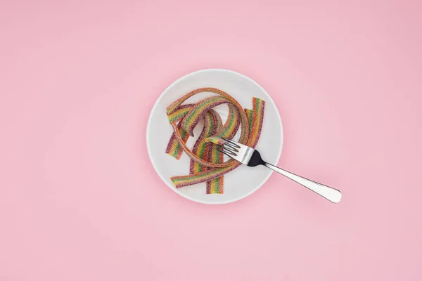 Vista dall'alto di caramelle di gelatina colorate piatte con zucchero e forchetta su piatto isolato su rosa — Foto stock