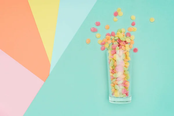 Vista superior de deliciosos caramelos de gelatina dispersos y vidrio en la superficie de color - foto de stock