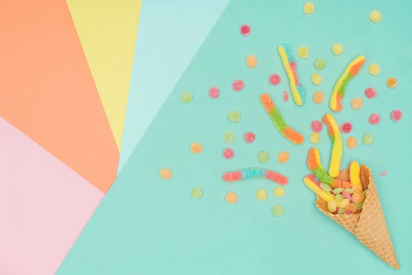 Вид сверху на разбросанные вкусные желейные конфеты и вафельный конус на цветной поверхности — стоковое фото