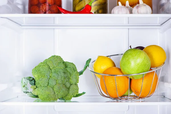 Broccoli and ripe tasty fruits in fridge — Stock Photo
