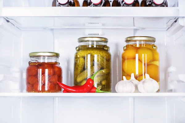 Preserved vegetables in glass jars and ripe chili peppers in fridge — Stock Photo