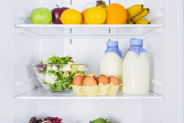 Oranges, apples, eggs and milk in bottles in fridge — Stock Photo
