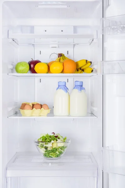 Frutta, bottiglie di latte e insalata in frigorifero — Foto stock