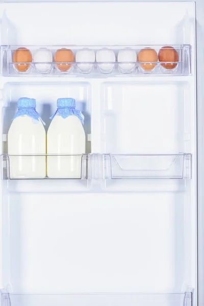 Chicken eggs and bottles of milk in fridge — Stock Photo