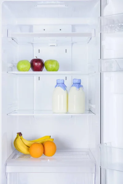 Pommes mûres savoureuses, bananes, oranges et bouteilles de lait au réfrigérateur — Photo de stock