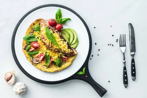 Composición de alimentos con tortilla saludable sobre tabla de madera y cubiertos sobre mesa de mármol blanco - foto de stock