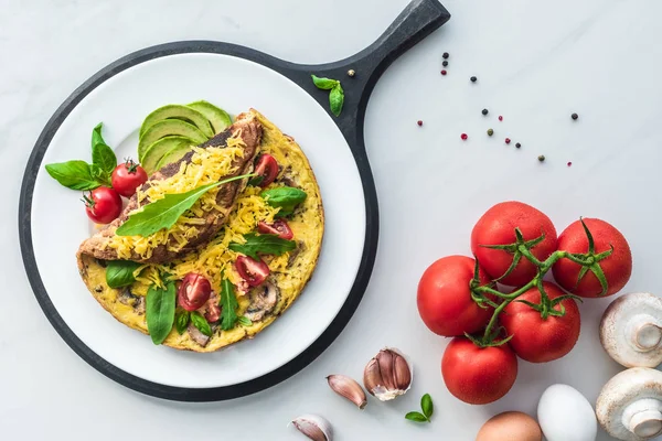 Food composition with healthy omelette on wooden board and ingredients on white marble tabletop — Stock Photo