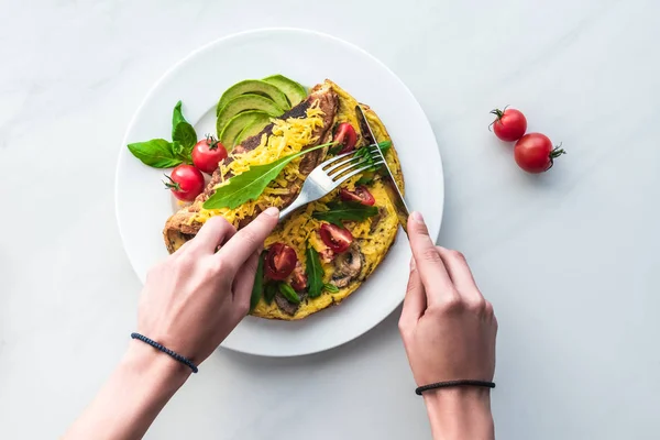 Teilansicht einer Frau, die hausgemachtes Omelett zum Frühstück an weißer Marmoroberfläche schneidet — Stockfoto