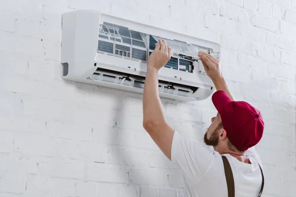 Jeune réparateur changeant de filtre pour climatiseur suspendu au mur de briques blanches — Photo de stock