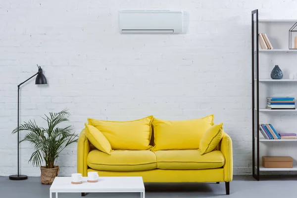 Interior de la moderna sala de estar con sofá amarillo y aire acondicionado colgando en la pared blanca - foto de stock
