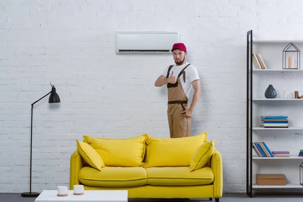 Profi-Reparateur steht neben Klimaanlage im Wohnzimmer und zeigt Daumen hoch — Stockfoto