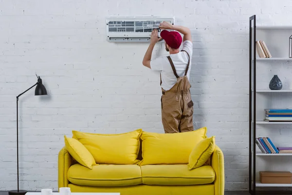 Reparador profissional fixando ar condicionado pendurado na parede de tijolo branco — Fotografia de Stock