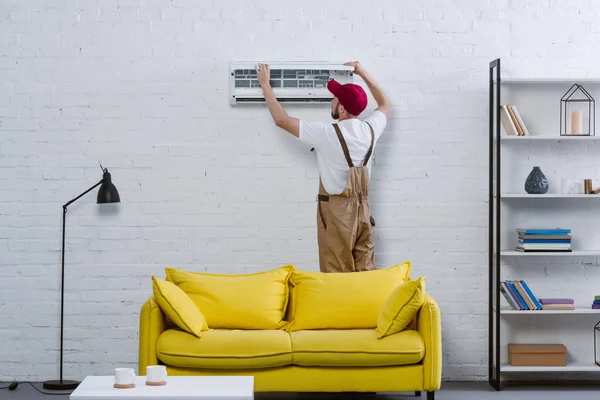 Jovem reparador profissional fixando ar condicionado pendurado na parede de tijolo branco — Fotografia de Stock